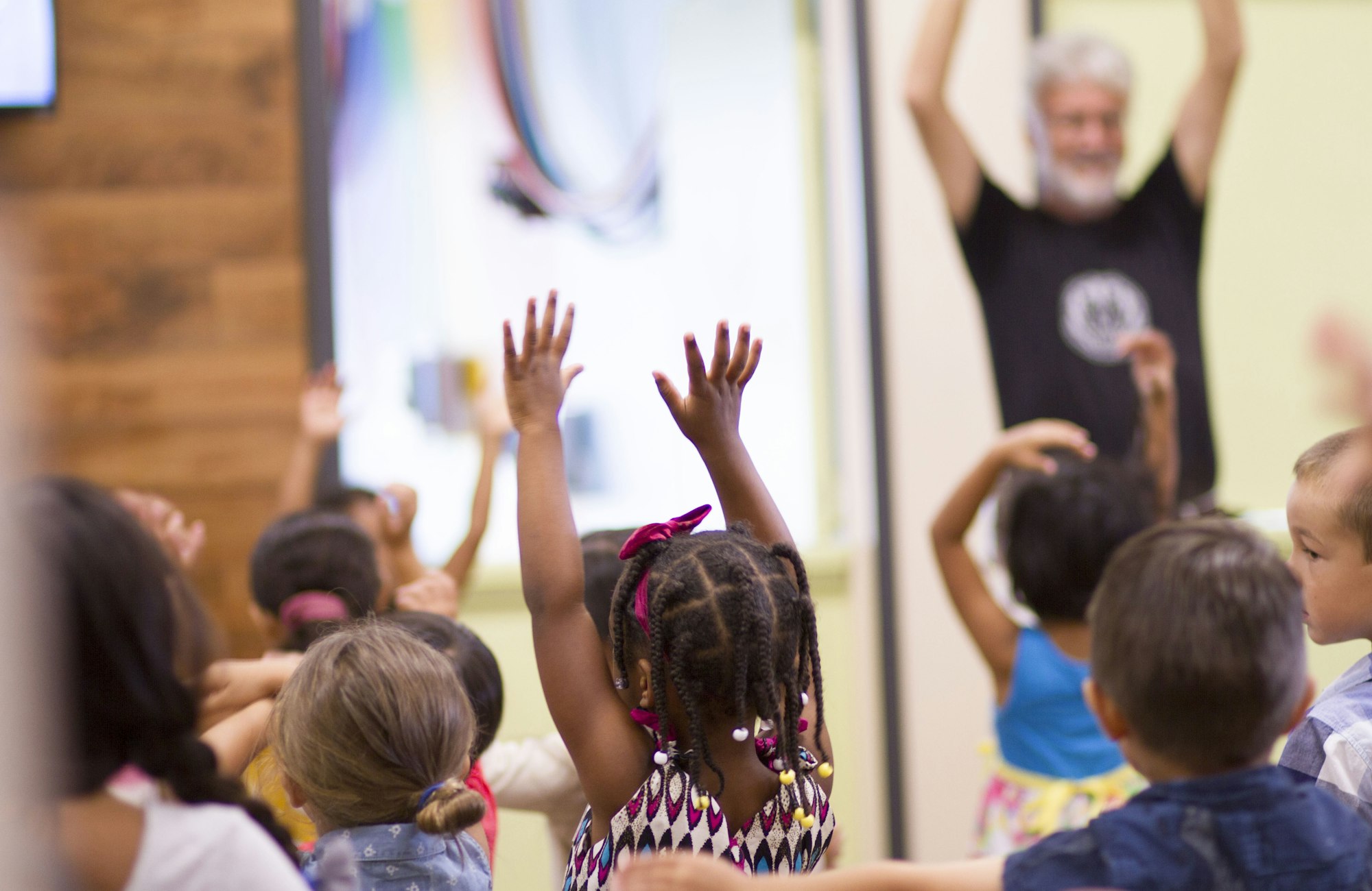 A room of children with their hands raised, singing during a kids worship service